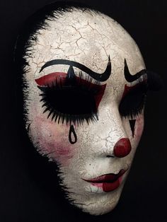 a white mask with black and red makeup on it's face is seen against a black background