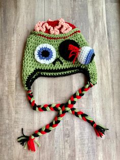 a crocheted hat with eyes and braids on the bottom, sitting on a wooden floor