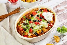 a white bowl filled with taco salad and tortilla chips on top of a wooden table