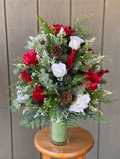 a vase filled with red and white flowers on top of a wooden table next to a wall