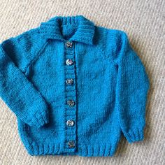 a blue sweater with buttons is laying on the floor next to a pair of scissors