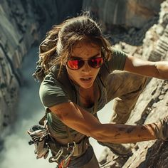 a woman climbing up the side of a mountain with her hands in the air and wearing red sunglasses