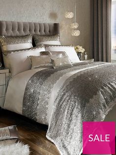 a bed with silver and white comforters in a bedroom next to a window,