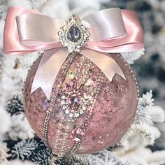 a pink ornament hanging from a christmas tree with a bow on it's side