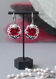 a pair of red and white beaded earrings sitting on top of a black stand