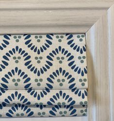 a blue and white patterned roman blind hanging in front of a wooden frame with an ornate pattern on it