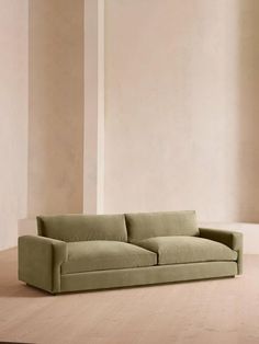 a green couch sitting on top of a hard wood floor next to a white wall