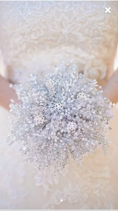 a woman in a wedding dress holding a silver brooch with snow flakes on it