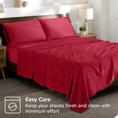 a bed with red sheets and pillows on top of it, next to a night stand