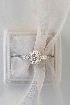 an engagement ring sitting on top of a white piece of cloth with a bow around it