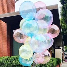 a bunch of balloons that are in the air near some bushes and trees on a sidewalk