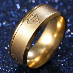 a gold ring with superman symbol engraved on the side and blue glitters in the background