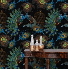 a table with two bottles on it next to a birdcage and peacock wallpaper