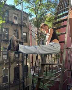 a woman standing on top of a metal hand rail next to a tall brown building