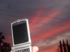 a person holding up a cell phone in front of the sky with power lines behind them