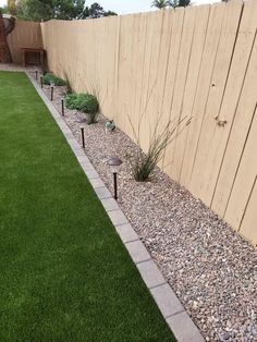 a backyard with grass, rocks and small plants in the ground next to a fence