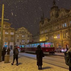 people standing in the snow near a street with a train on it's tracks