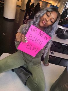 a woman sitting on the ground holding a pink sign that says irr nen blch at bum