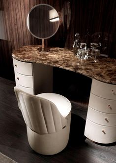 an elegant vanity with marble top and curved chair in front of it, next to a round mirror