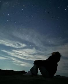 a person sitting on the ground looking up at the sky with stars in the background