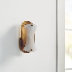 a white and gold wall light mounted on the side of a wall next to a window