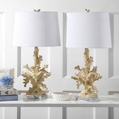 two gold coral lamps sitting on top of a white table next to a blue book