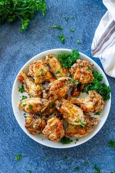 a white bowl filled with chicken wings and garnished with parsley on a blue surface