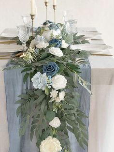 the table is decorated with blue and white flowers, greenery and silver candlesticks