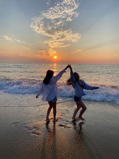 two girls are playing on the beach at sunset