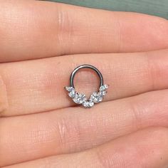 a person is holding an open nose ring with three small leaves on the end of it