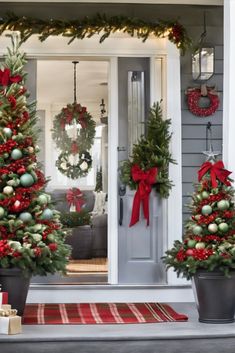 three christmas trees are decorated with red and green ornaments on the front porch, along with wreaths