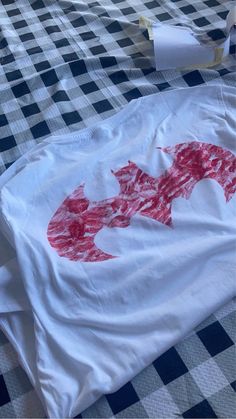 a white t - shirt with red designs on it sitting on a checkered table cloth