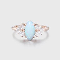 an opal and diamond ring with three pear shaped diamonds on the side, set in 18k rose gold