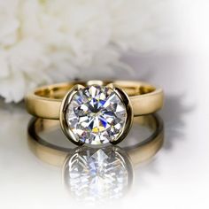 two yellow gold wedding rings with a diamond in the center and white flowers behind them