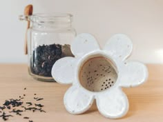 a white flower shaped tea strainer sitting on top of a wooden table next to a jar