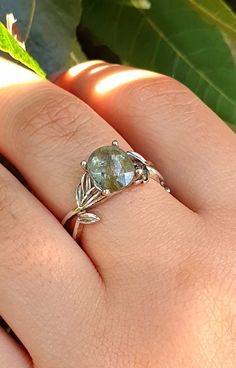 a woman's hand holding a ring with a green stone in the middle and leaves around it