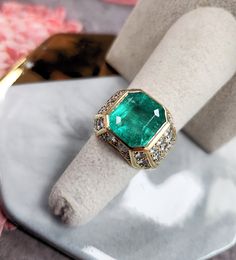 an emerald and diamond ring sitting on top of a table