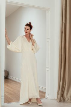 a woman in a white dress is talking on her cell phone while standing in an empty room