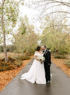 a bride and groom kissing on a path surrounded by trees with leaves all around them