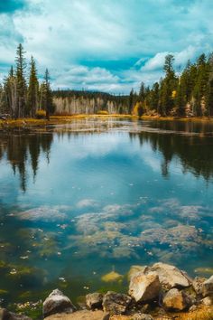 a lake surrounded by rocks and trees under a cloudy blue sky with clouds in the background