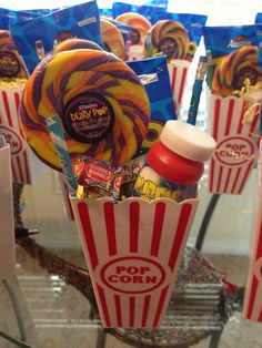 popcorn buckets filled with candy and lollipops on top of a glass table