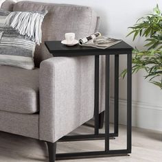 a small table with a magazine on it next to a couch and potted plant