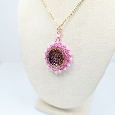 Add a touch of elegance and charm to your outfit with this beautiful handmade beadwork glass pendant!  Hand woven pendant features a stunning Czech pressed glass rosette cabochon surrounded by intricate beadwork featuring fine Miyuki glass seed beads and sparkling crystal rondelle beads. The pendant hangs delicately from a Gold-plated Stainless Steel chain. Whether you're dressing up for a special occasion or simply adding a pop of color to your everyday look, this pendant is sure to turn heads and spark joy wherever you go!  Each piece is lovingly crafted by hand, making it a unique and special addition to your jewelry collection. Treat yourself or surprise a loved one with this one-of-a-kind piece that is sure to gather compliments! 👉  Hand beaded by CyntheCreations 👉  Measurements:  1 Pink Round Jewelry With Bead Caps, Czech Glass Beaded Jewelry Gift, Artisan Beaded Round Pendant Jewelry, Beaded Czech Glass Cabochons For Jewelry Making, Beaded Czech Glass For Jewelry Making, Pink Beaded Flower Pendant Jewelry, Beaded Chain Medallion Jewelry Gift, Pink Beaded Flower Pendant Necklace, Bohemian Beaded Necklaces With Cabochon For Gifts