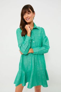 a woman in a green shirt dress posing for the camera with her hands on her chin