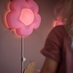 a pink flower shaped lamp sitting on top of a table next to a woman's face