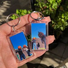 two key chains with pictures of people on them in front of a plant and potted plants