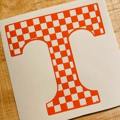 an orange and white checkered letter t sticker on a wooden table with scissors