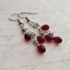 Bloodstone Red Czech Glass Cluster Drop Earrings in Antiqued Silver EARRINGS ONLY Such a rich gothic garnet or bloodstone red! Please note: Bringing them into light draws out the red, otherwise they can almost appear black.  I wrapped garnet Czech glass teardrop beads in titanium wire and minimally suspended three from a length of antiqued silver chain to form a delightful cluster dangle. Earrings fall from your choice earwires.   Earrings can appear almost black in the shadows but light brings out the glorious shades of red.  For clarification, these are not gemstones but Czech glass.  Want a full ensemble?? Add on the pendant in the same bloodstone red/garnet Czech glass as seen in a few of these images. https://www.etsy.com/listing/1157131359/garnet-red-cluster-pendant-necklace REPEAT C Red Teardrop Chandelier Earrings, Red Teardrop Chandelier Earrings With Ear Wire, Red Nickel-free Chandelier Earrings As Gift, Red Wire Wrapped Dangle Earrings, Red Gothic Earrings For Pierced Ears, Red Wire Wrapped Metal Earrings, Gothic Red Nickel-free Earrings, Antique Silver Earrings, Earrings Fall