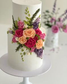 there is a white cake with pink and orange flowers on the top, next to two small vases