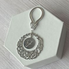 a white box with a metal keychain on top of it that has a silver medallion in the middle